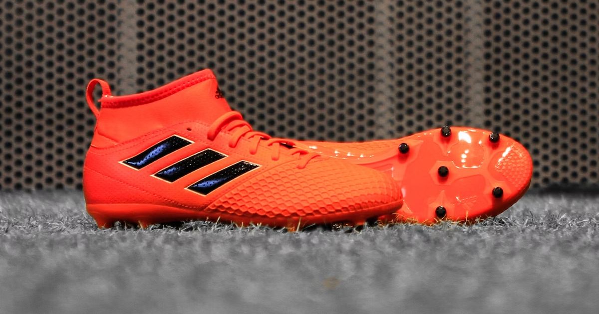 A pair of orange adidas football boots with extended fabric collars and black stripes down the sides sat on grey artifical turf.