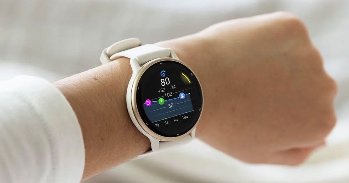 Someone in a white top wearing a white-strapped golden smartwatch with a black screen with activity information on it.