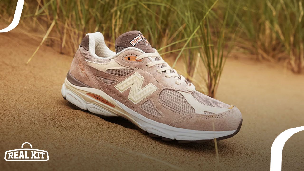 A sandy orange, yellow, and pinkish New Balance shoe sat on sand in front of tall, thin grass.