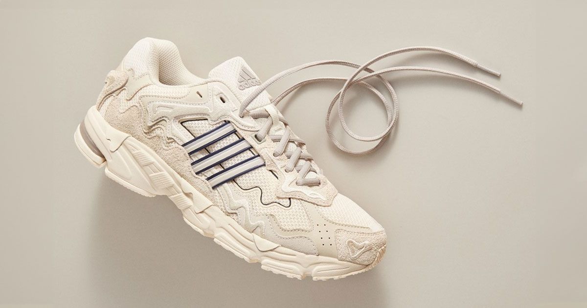 A cream and off-white low-top shoe with its laces undone, featuring grey stripes on the sidewall with black outlines.