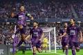 Image of a team dressed in purple celebrating a goal inside a stadium.