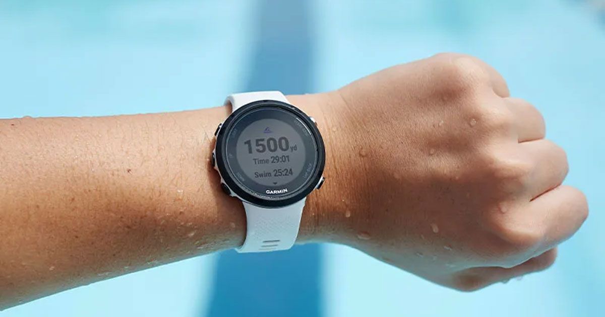 Image of a Garmin Swim 2 watch with a white strap on a wrist of someone standing by a pool.