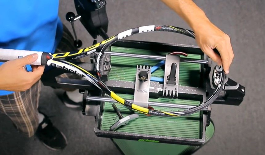 Image of a black, yellow, and white Babolat tennis racquet being secured into a black stringer machine.
