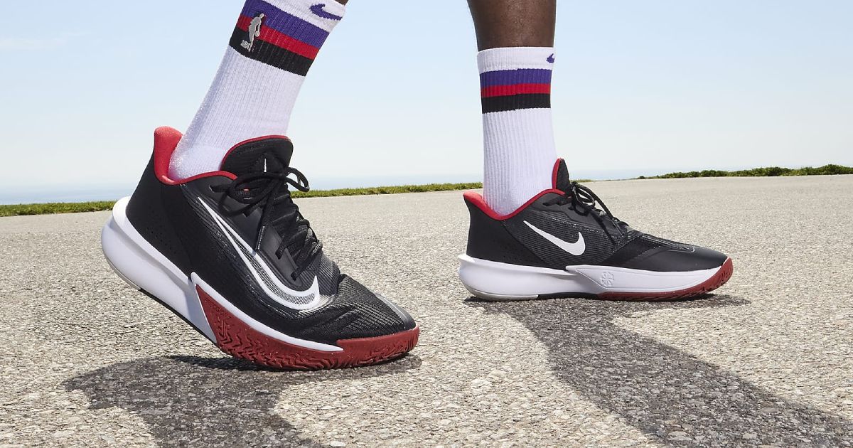 Someone in white Jordan socks with purple, red, and black trim wearing a pair of black, white, and red Nike Precison 7 sneakers.