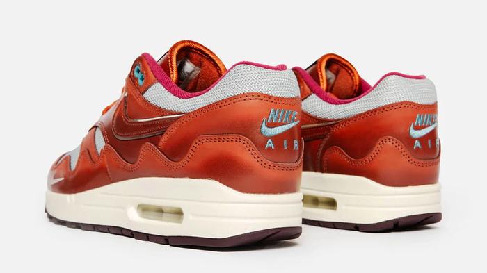 Patta x Nike Air Max 1 product image of a burnt orange and grey pair of sneakers on feet.