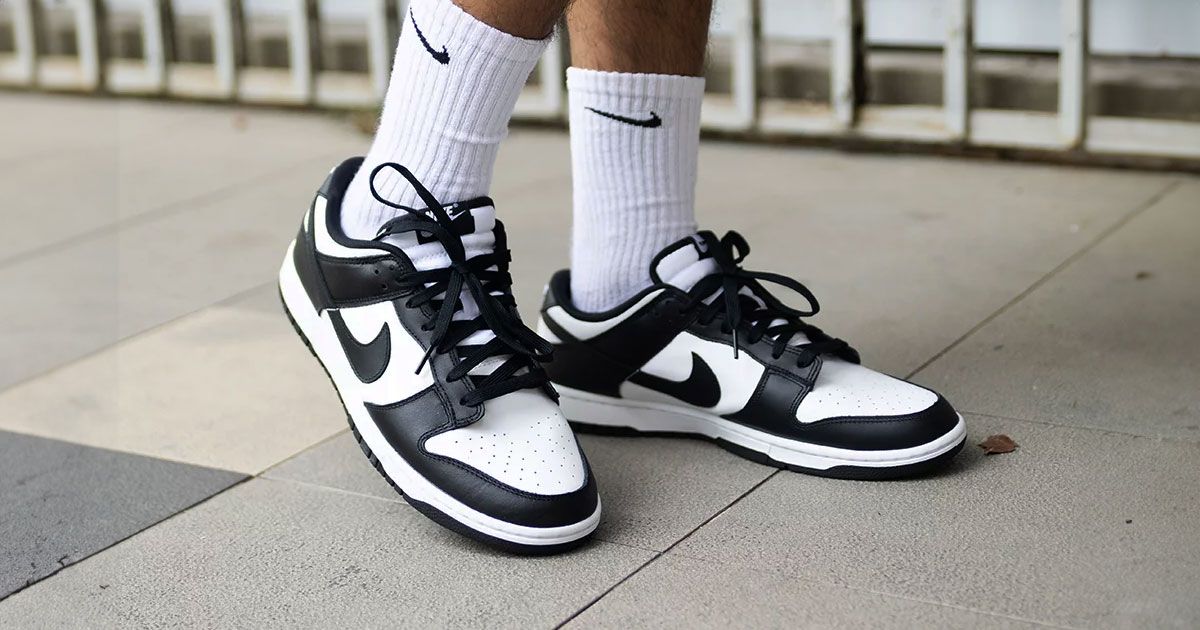Someone in white Nike-branded socks wearing a pair of white and black Nike Dunk Lows.