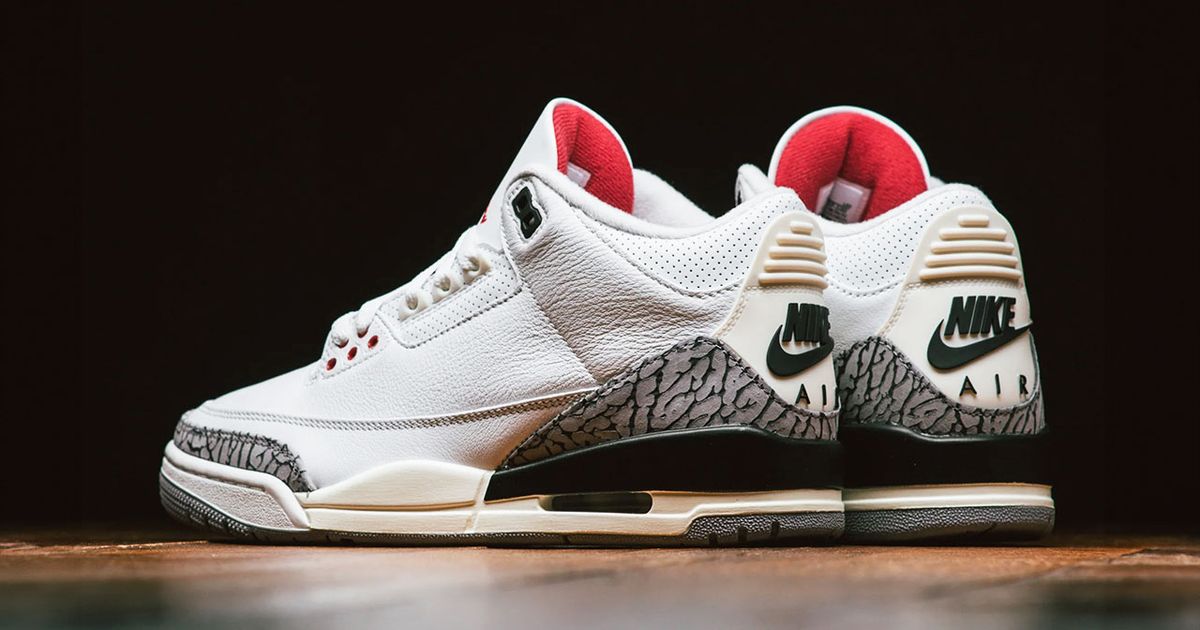 A shot of the back and side of a pair of white Air Jordan 3s with red interiors, black branding, and elephant print on the heels.