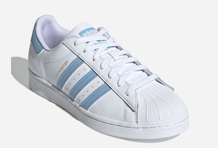 adidas Superstar product image of a white sneaker with light blue and gold details.