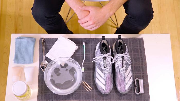 adidas' cleaning setup for cleaning football cleats featuring a brush, toothbrush, and a bowl of water.