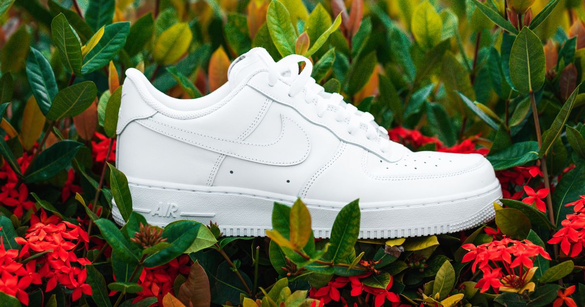 An all-white Air Force 1 Low laying in a bed of red flowers.
