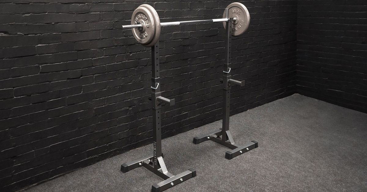A black squat rack with a barbell and weight plates on top, the rack in a black brick room featuring a grey floor