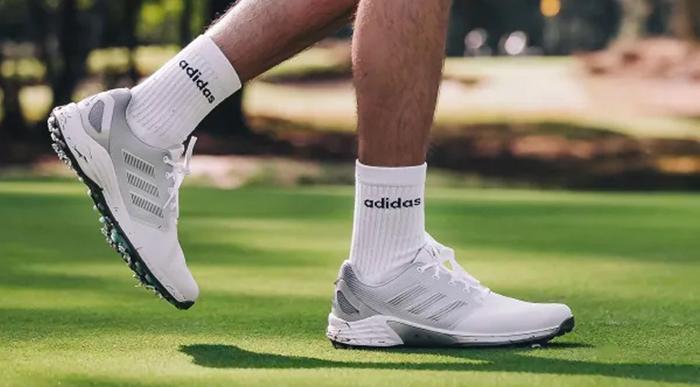 Best golf shoes adidas product image of a pair of white trainers that fade into a dark green with yellow details.