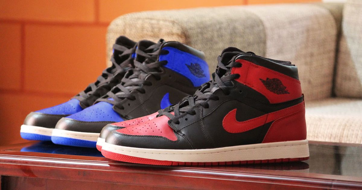 Two Air Jordan 1 pairs, one in red and black, the other in blue and black, both sat on a wooden table.