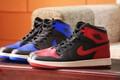 Two Air Jordan 1 pairs, one in red and black, the other in blue and black, both sat on a wooden table.