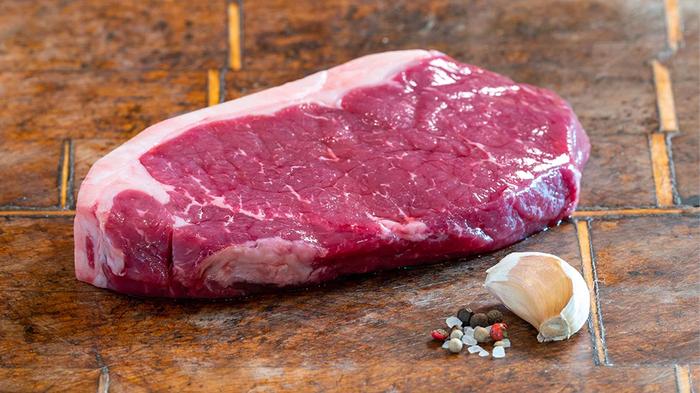 Image of a raw grass-fed beef sirloin steak next to garlic.