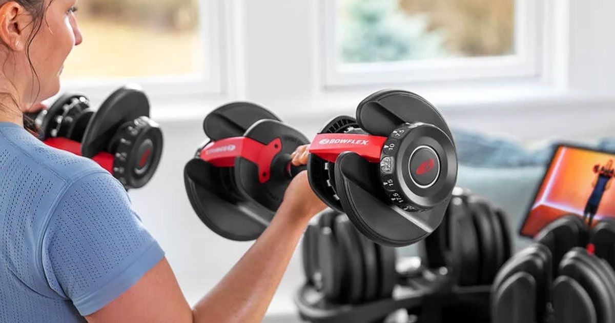 Someone in a blue t-shirt lifting a set of black adjustable dumbbells with red trim.