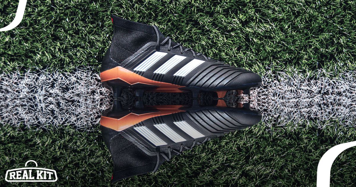 A pair of black adidas boots with bronze details and white stripes down the side laying on the white line on a pitch.
