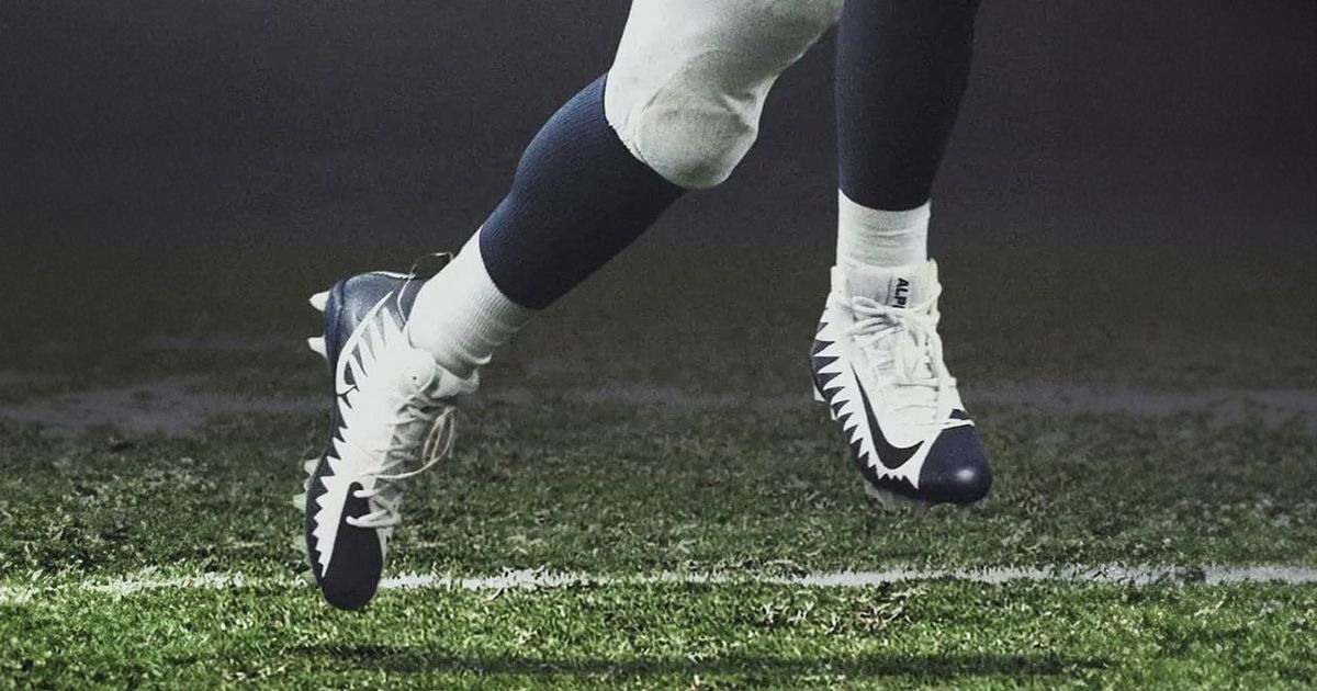 Someone in full football gear wearing a pair of black and white Nike cleats.