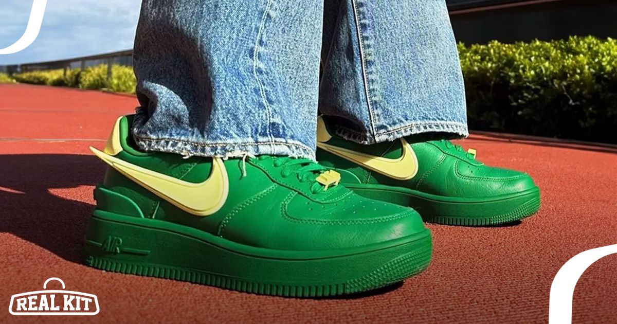 Someone in light blue jeans standing on an orange surface wearing a pair of bright green Nike Air Force 1s featuring yellow Swooshes.