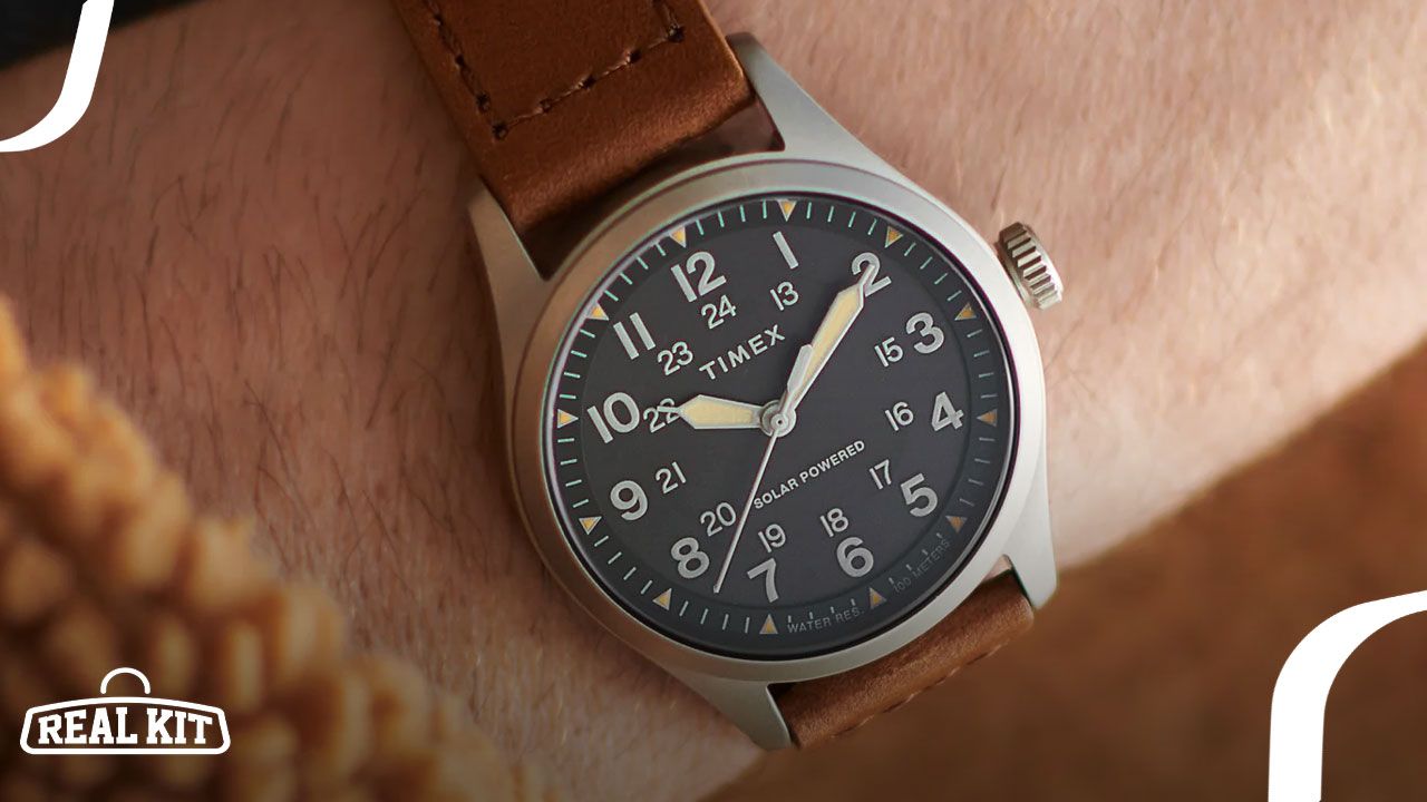 Close-up of someone wearing a silver analogue watch with a black watch face and brown strap.