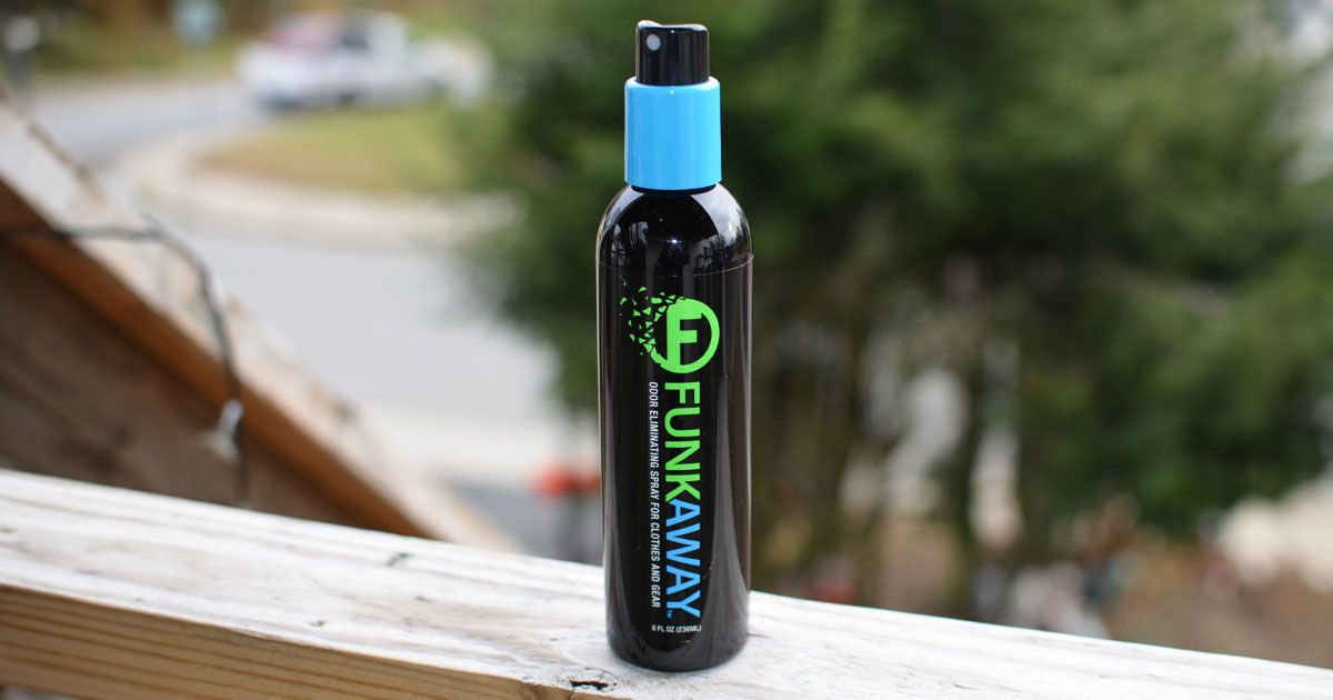 A black sprayable bottle with a blue cap and blue and green branding sitting on top of a wooden fence.