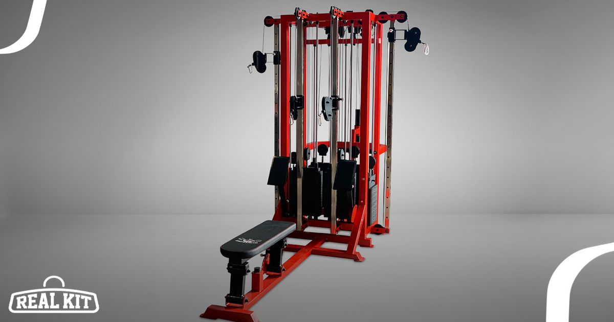 A red and black gym cable machine with a bench attached in a grey room.