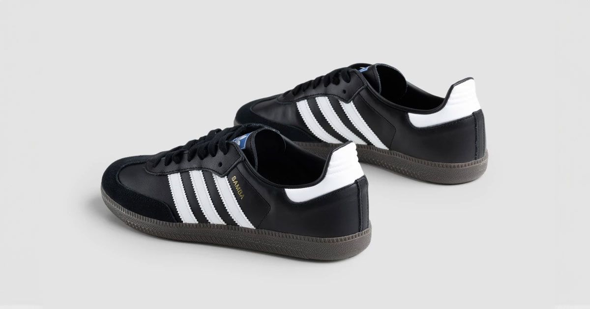 A pair of black adidas shoes featuring three white adidas stripes down the sides, white heel sections, and blue logos on the tongues.