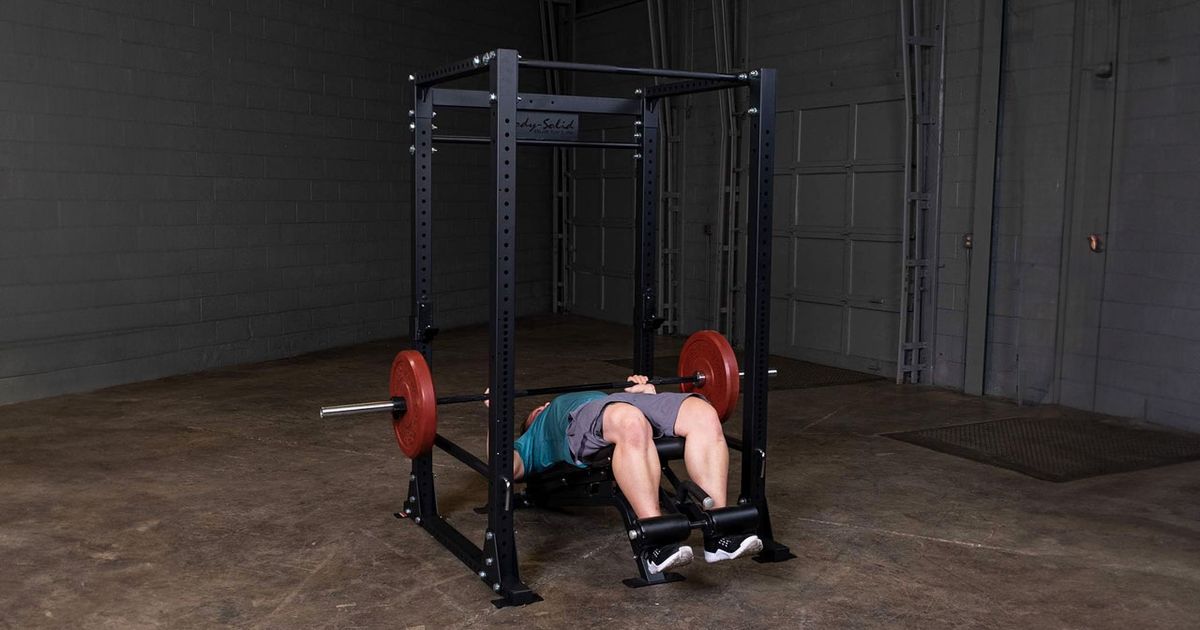 A black four-sided power cage with someone in a blue shirt and grey shorts performing a decline bench press.