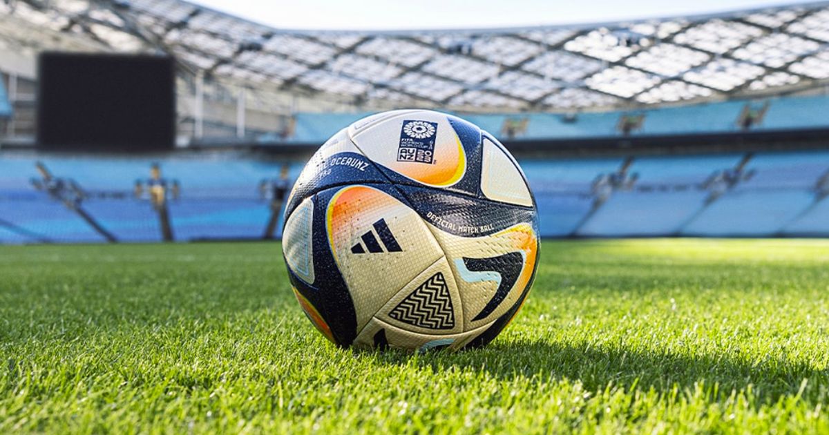 A gold and black football featuring hits of light blue and orange across the surface sat on a grass pitch.