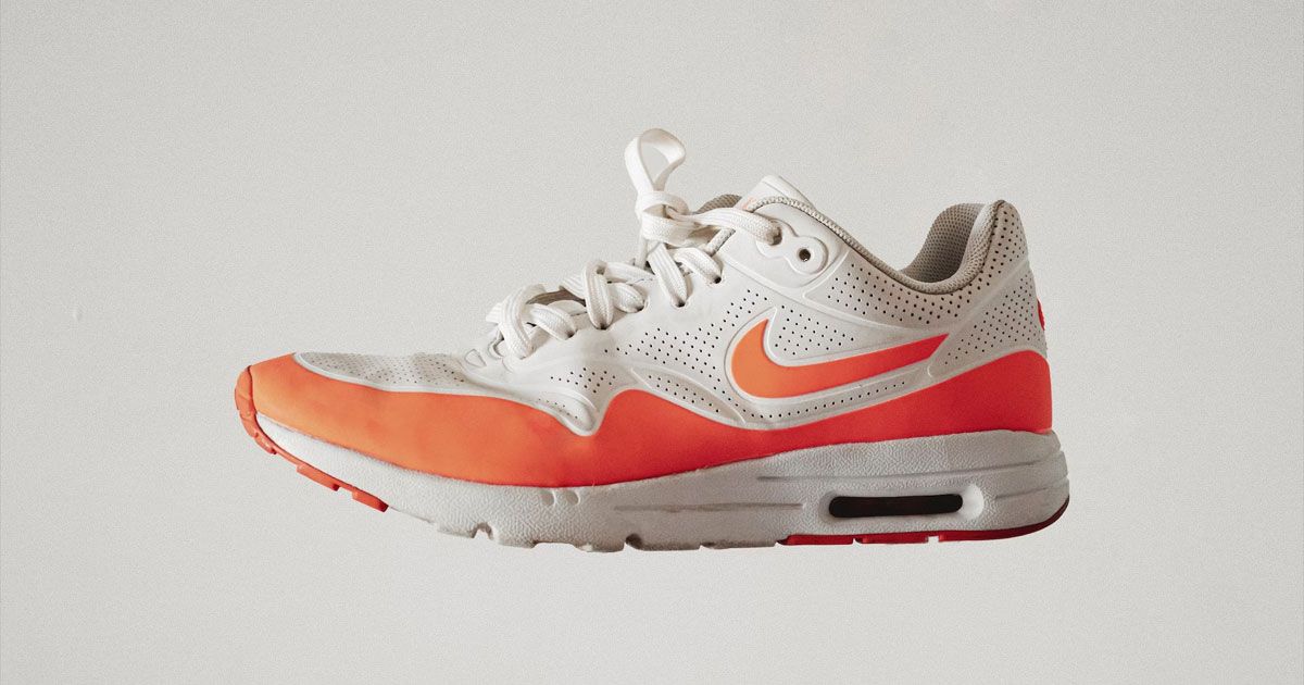 A light cream Nike Air Max featuring an orange mudguards, heel, and Swoosh on the side.