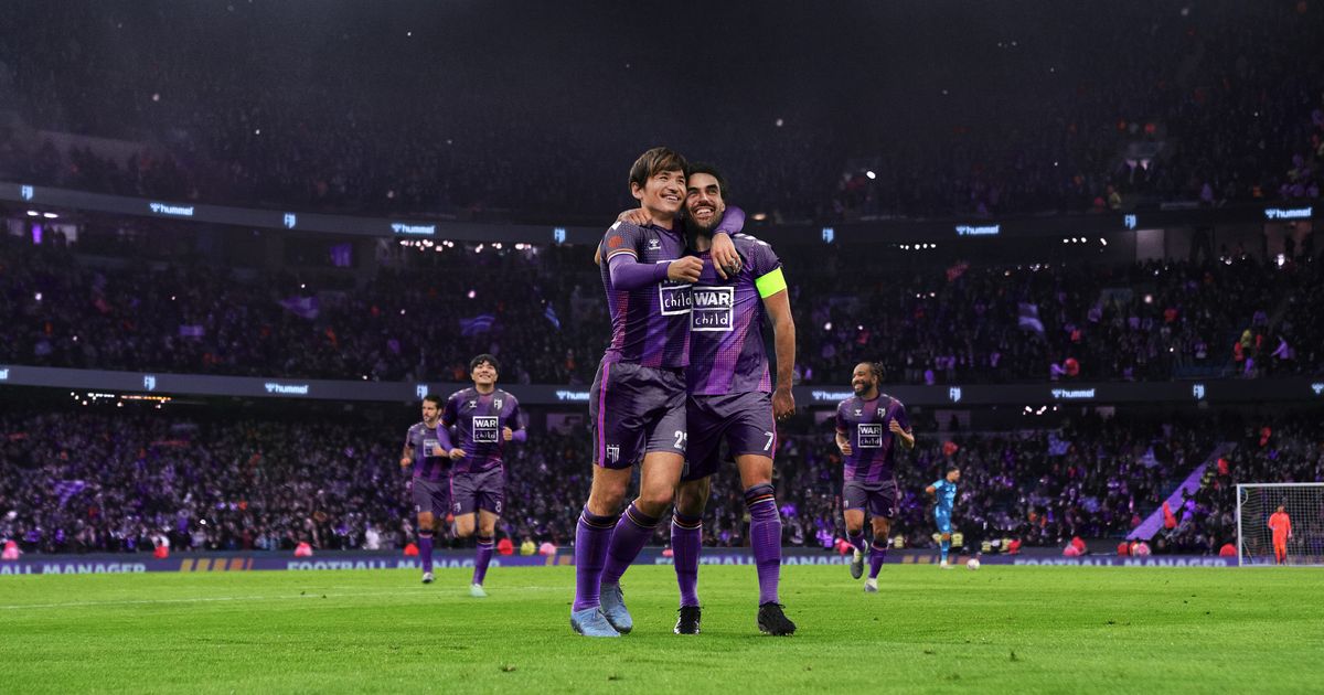 Two football players in purple kits celebrating inside a packed stadium.