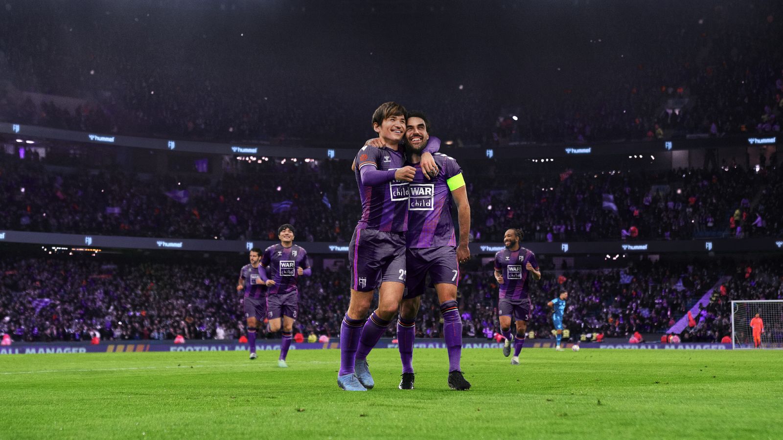 Two football players celebrating in purple kits in the middle of a stadium.