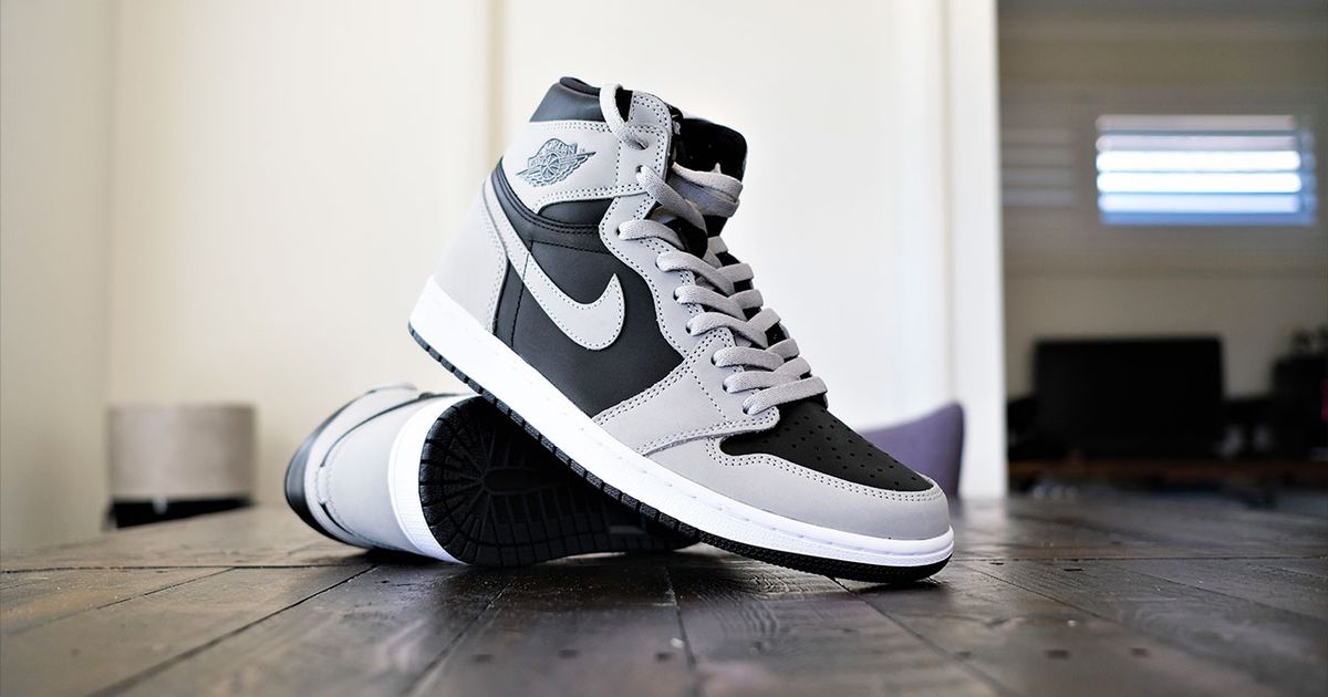 A pair of grey, black, and white Jordan 1s, with on its side and the other propped up against it.