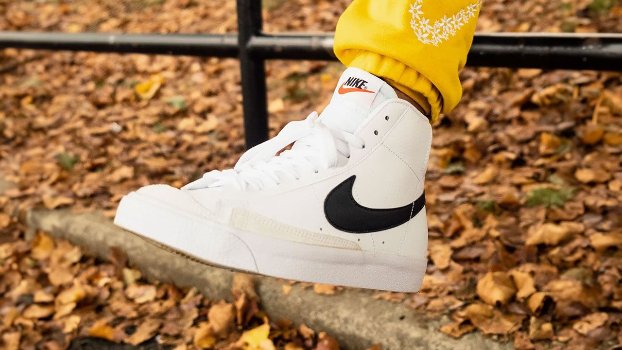 Someone in yellow joggers wearing a white Nike Blazer Mid featuring a black Swoosh down the side.