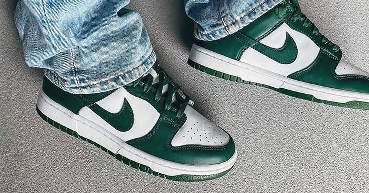 Someone in light blue jeans wearing a pair of white and dark green Nike Dunk Lows.