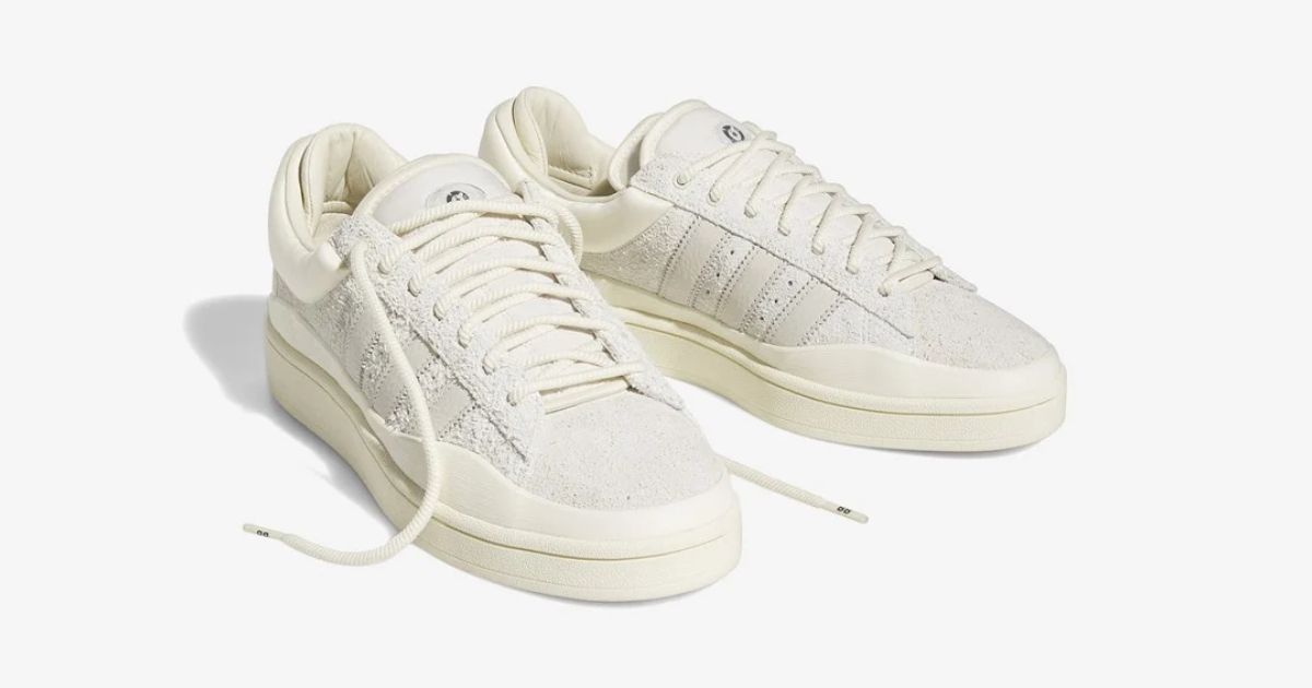 A pair of low-top, cream adidas sneakers with each shoe's laces untied.