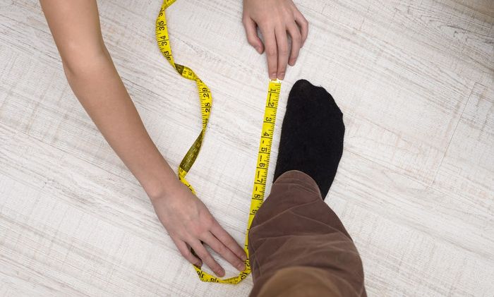 Image of someone measuring a foot with a yellow tape measure.