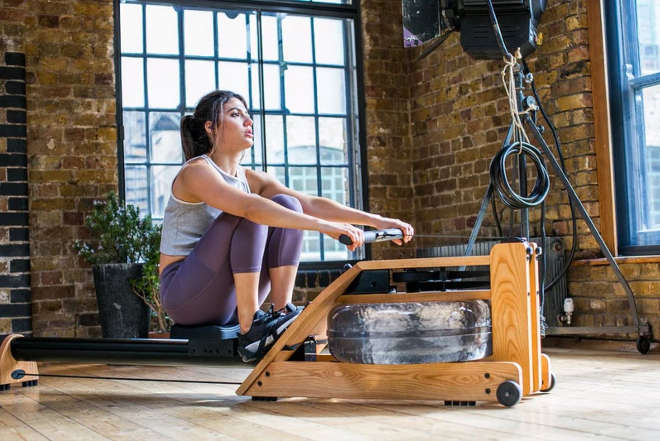 Someone in a grey top and purple leggings using a wooden water rowing machine.