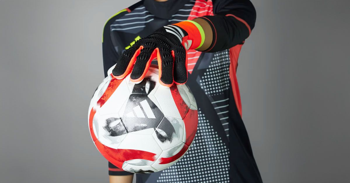 Someone in black and orange goalkeeper gloves holding a white, black, and orange football in one hand.