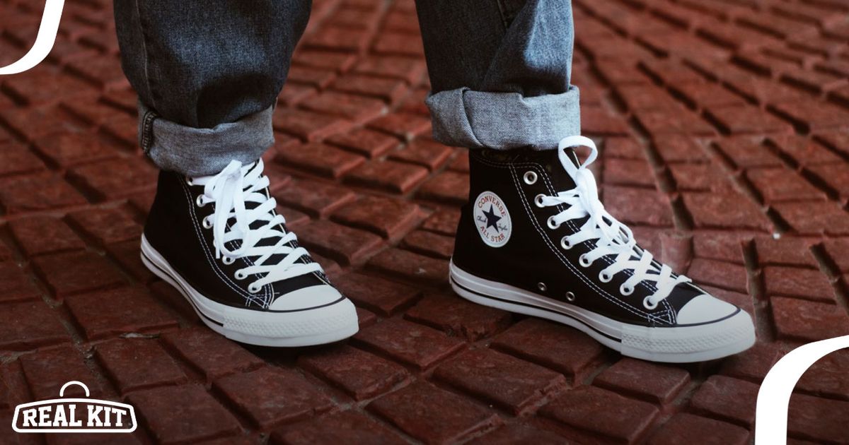 Image of a black and white pair of Converse high-tops on-feet of someone in rolled-up jeans.