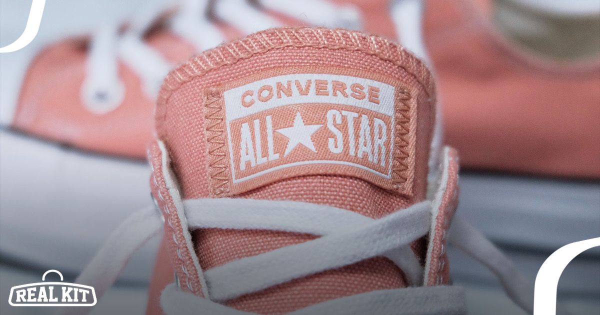 Close-up shot of the tongue and branding on a pink Converse sneaker with white laces.