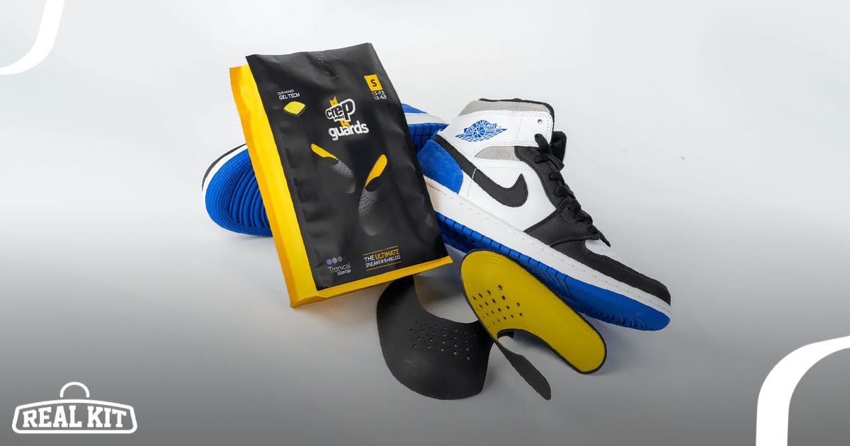 A black and yellow packet laying on a pair of white, blue, and black Jordan 1s and next to a yellow and black pair of crease protectors.