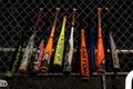 Image of 10 different coloured baseball bats lined up on a wired fence.