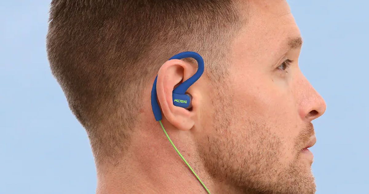 A blue wired earbud with an over-ear loop in the ear of someone with short brown hair.