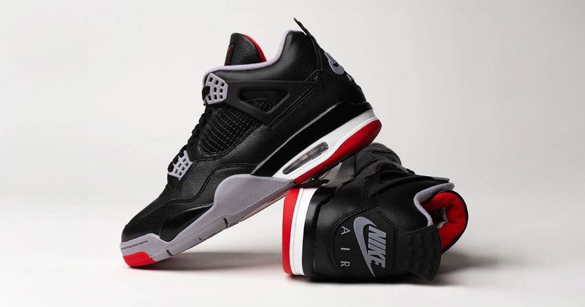 A pair of black leather Jordan 4s, one of its side, the other leaning against it. Both sneakers featuring grey, red, and white accents.