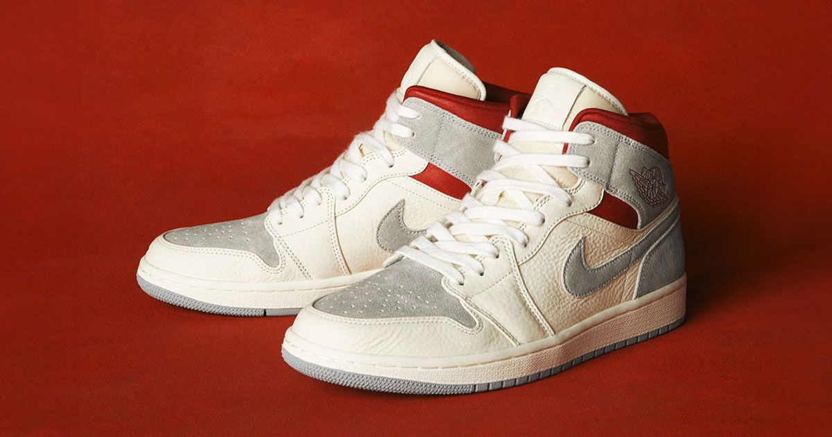 A pair of predominately white Jordan 1s featuring suede grey and red panels and details.