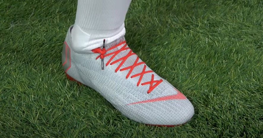 A white Nike football boot with red laces tied to the side and tucked into the boot.