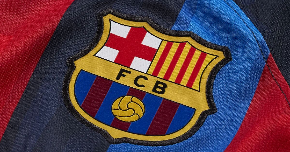 A close-up of the yellow Barcelona badge on the blue and red striped jersey, the badge featruing a red cross in the top left, and yellow and red stripes in the right.
