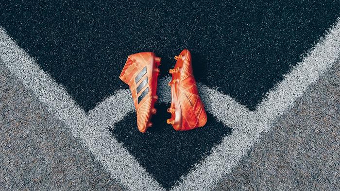 A pair of bright orange adidas football boots laying at the corner of a football pitch.