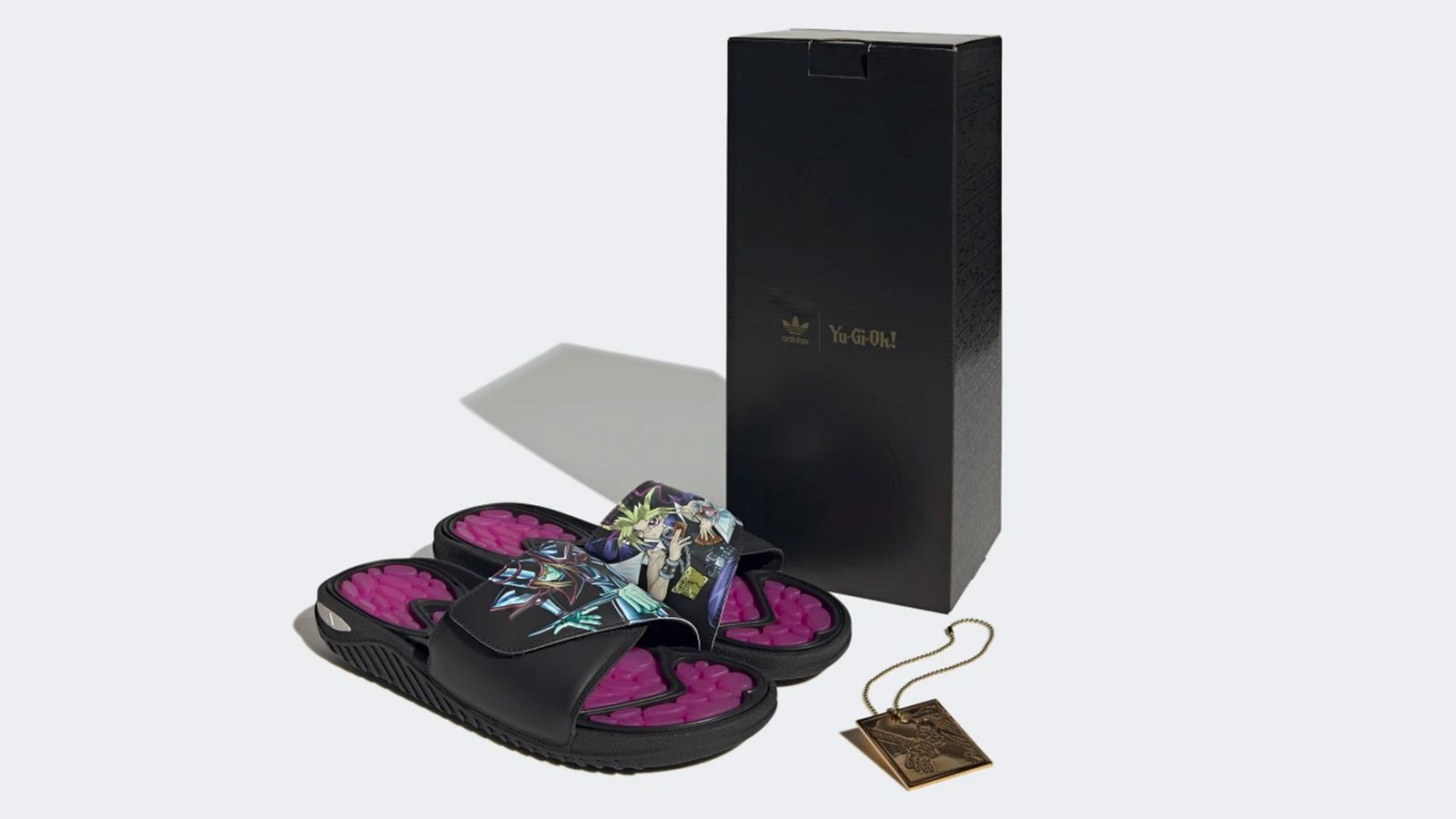 Yu-Gi-Oh! x adidas Reptossage Slides product image of black and purple sliders with graphics of Dark Magician and Yugi on top next to their black custom box.